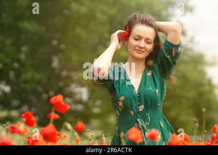une jeune femme blanche insère une fleur rouge dans ses cheveux sur un champ de pavot, son visage est éclairé par les rayons du soleil, l'atmosphère de vacances, voyage Banque D'Images