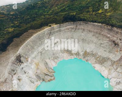 Vue aérienne du lac turquoise d'eau de soufre, entouré par une falaise rocheuse au volcan Kawah Ijen à Java est, Indonésie. Banque D'Images