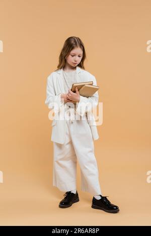 concept d'éducation, préadolescence fille en costume blanc tenant des livres et debout sur fond beige, tenue à la mode, tenue formelle, retour à l'école, prepas Banque D'Images