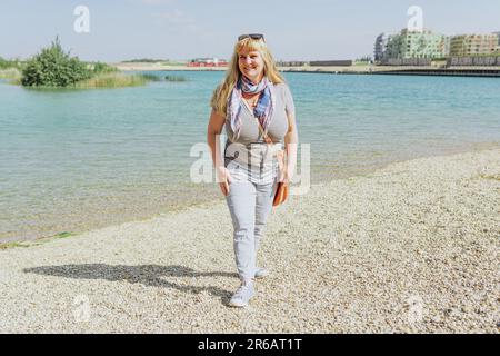 Portrait femme d'âge moyen attrayante de formes de plumeuses sur le rivage de la mer ou du lac Banque D'Images