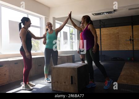 Des amies multiraciales gaies donnant des cinq hauts lorsqu'elles sont debout près de la boîte de PLYO dans le club de santé Banque D'Images