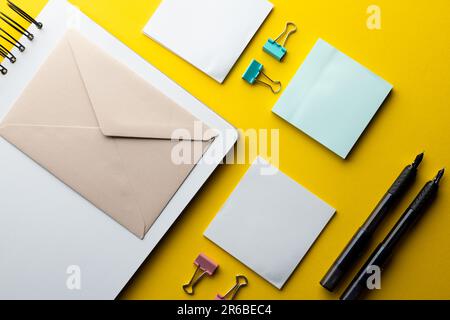 Pose à plat de stylos noirs, d'enveloppes et de papier blanc avec espace de copie sur fond jaune. Matériel scolaire, écriture, coloriage, dessin, apprentissage, école Banque D'Images