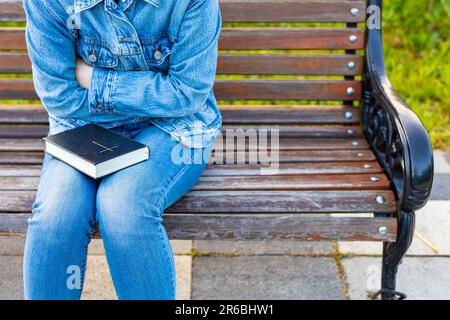 femme tenant une bible assise sur un banc.bible fermée dans les mains. la bible se trouve sur les genoux de la fille Banque D'Images