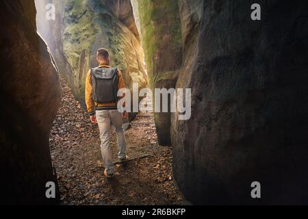 Homme avec sac à dos marchant sur un sentier étroit entre les colonnes de pierre naturelle dans les rochers de grès. Hruba Skala dans le Paradis tchèque. Banque D'Images