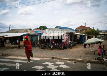 Tanzanie, Afrique - 14 mars 2023: Marché rural de village avec de nombreuses motos garées à l'extérieur, comme un homme Masaai guerrier traverse la route Banque D'Images