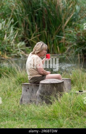 Cratère de Ngorongoro, Tanzanie - 12 mars 2023 : une femme touristique est assise sur une souche, buvant d'une tasse en plastique rouge, pendant le safari Banque D'Images