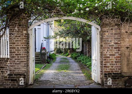 Vue sur une allée à travers une porte ouverte vers la route de gravier à deux voies le long du côté d'une maison avec un peu de lumière du soleil. Banque D'Images