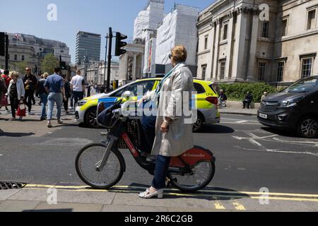 Femme avec imperméable sur le vélo Santander, Charing Cross, West End de Londres sur une chaude journée d'été pendant une mini-canicule en juin 2023, Londres, Angleterre, Royaume-Uni Banque D'Images