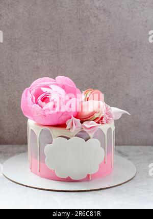 Gâteau gris élégant décoré de chocolat blanc fondu, macarons, fleur de pivoine rose comestible, petits gâteaux et meringues avec espace pour le texte Banque D'Images