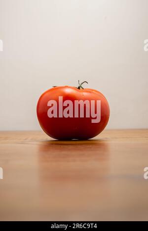 Goiania, Goias, Brésil – 08 juin 2023 : une tomate rouge mûre sur une table rustique en bois, avec un fond blanc neutre. Banque D'Images