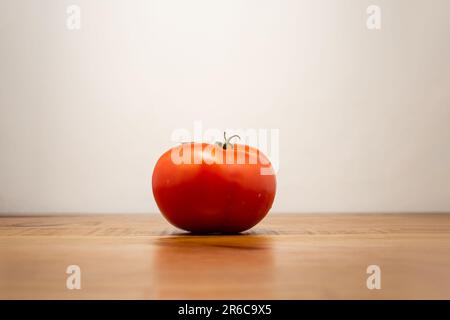 Goiania, Goias, Brésil – 08 juin 2023 : une tomate rouge mûre sur une table rustique en bois, avec un fond blanc neutre. Banque D'Images