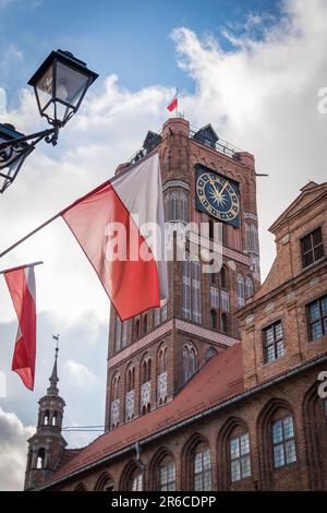 Deux drapeaux polonais accrochés à la tour ratusz de l'hôtel de ville de Torun en arrière-plan à Torun, en Pologne. Banque D'Images