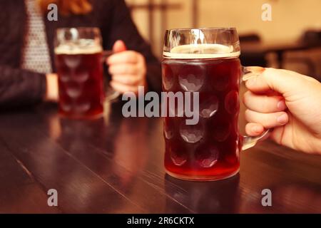 Dans un cadre de pub confortable, deux amis apprécient une tasse rafraîchissante de bière légère. Leurs mains lèvent les verres stein de bière et les clink doucement Banque D'Images