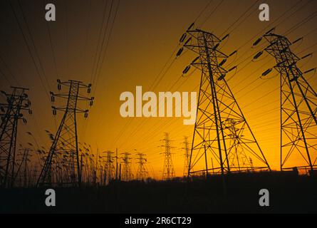 Lignes haute tension transportées par des tours en acier silhouetées au coucher du soleil Banque D'Images