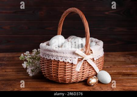 Panier en osier avec des œufs de Pâques décorés avec soin et des fleurs de lilas blanc sur une table en bois Banque D'Images