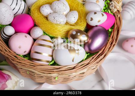 Panier en osier avec œufs de Pâques décorés avec soin sur une table en marbre blanc, vue ci-dessus Banque D'Images