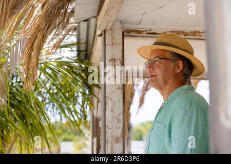 Vue latérale d'un homme âgé caucasien attentionné portant un chapeau debout sur le balcon du cottage Banque D'Images