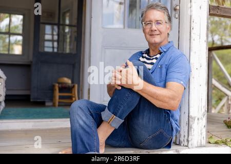 Portrait d'un homme âgé caucasien habillé en casual assis sur des marches à l'extérieur de la maison Banque D'Images