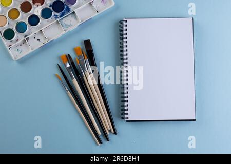 Gros plan des peintures, des carnets et des pinceaux avec espace de copie sur fond bleu. Retour à l'école, art, peinture, matériel scolaire, apprentissage, école et edu Banque D'Images