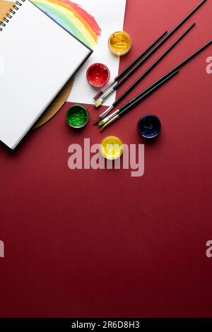 Gros plan sur les peintures, les pinceaux et le bloc-notes avec un espace de copie sur fond rouge. Retour à l'école, art, peinture, matériel scolaire, apprentissage, école et educ Banque D'Images