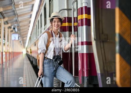 Une belle et positive jeune femme de voyage routard asiatique embarque dans le train à la gare. Vacances d'été, voyage seul, vacances Banque D'Images