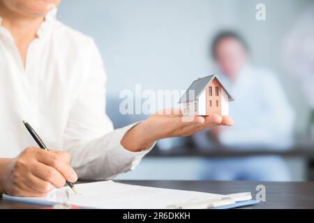 Femme d'affaires choisissant mini modèle de maison de modèle sur table en bois, planification pour acheter la propriété. Concept de choisir le meilleur. Banque D'Images