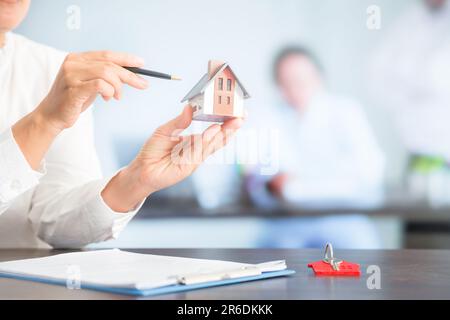 Femme d'affaires choisissant mini modèle de maison de modèle sur table en bois, planification pour acheter la propriété. Concept de choisir le meilleur. Banque D'Images