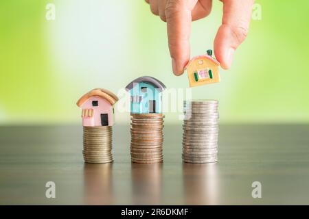 Femme main tenir un modèle de maison mis sur la pièce de pile avec la croissance dans le parc public, l'argent d'épargne pour acheter maison et prêt à l'investissement d'affaires pour re Banque D'Images