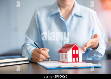 Femme d'affaires choisissant mini modèle de maison de modèle sur table en bois, planification pour acheter la propriété. Concept de choisir le meilleur. Banque D'Images