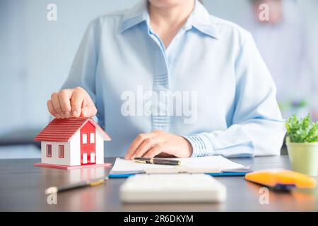 Femme d'affaires choisissant mini modèle de maison de modèle sur table en bois, planification pour acheter la propriété. Concept de choisir le meilleur. Banque D'Images