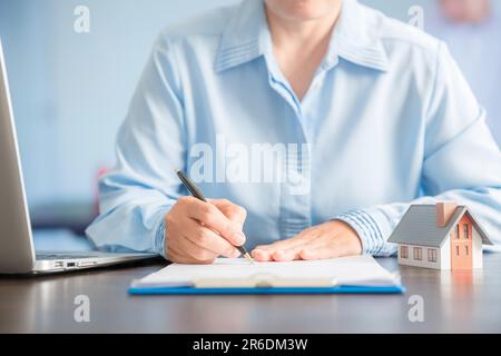 Femme d'affaires choisissant mini modèle de maison de modèle sur table en bois, planification pour acheter la propriété. Concept de choisir le meilleur. Banque D'Images
