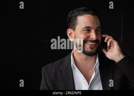 Portrait d'un homme d'affaires beau sur fond noir souriant et parlant sur téléphone photo horizontale Banque D'Images