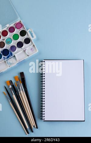 Gros plan des peintures, des carnets et des pinceaux avec espace de copie sur fond bleu. Retour à l'école, art, peinture, matériel scolaire, apprentissage, école et edu Banque D'Images