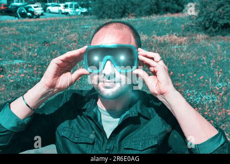 Jeune homme de la nature portant des lunettes de réalité augmentée. Homme adulte s'amusant avec des lunettes AR. Lecture. Jour. Banque D'Images