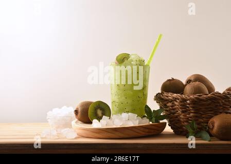 Détail de la boisson froide au kiwi avec beaucoup de glace sur un banc de cuisine en bois avec des fruits coupés et un bol avec de la glace autour de son arrière-plan isolé. Vue avant. Hé Banque D'Images