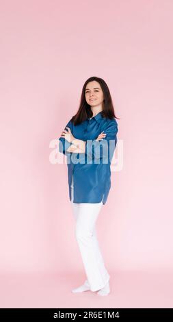Portrait de femme d'affaires professionnelle en tenue décontractée intelligente debout avec confiance avec les mains pliées, isolé sur un fond rose, vertical Banque D'Images