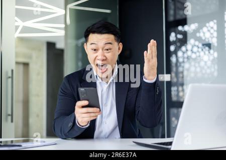 Un homme d'affaires asiatique couronné de succès a reçu une bonne notification en ligne, le patron du lieu de travail a tenu main haute pour célébrer les succès et les victoires. Banque D'Images