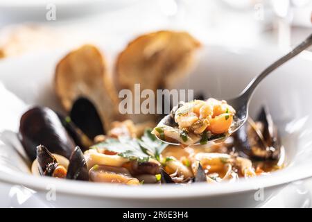 Crevettes sur une cuillère prise d'une soupe de fruits de mer dans une assiette. Banque D'Images