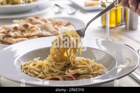 Main avec une fourchette de spaghetti aglio e olio peperoncino d'une assiette dans un restaurant. Banque D'Images