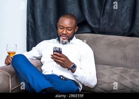 Homme d'affaires se détend sur un canapé tenant un verre de vin et utilisant un smartphone pour la communication Banque D'Images