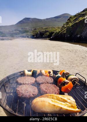 Faire un barbecue sur une plage de sable entourée de montagnes à Silver Strand, Thallabawn, Doovilra, Louisburgh, Co Mayo, Irlande Banque D'Images