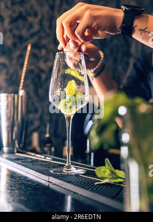 Barman mettre les feuilles de menthe dans le verre, il prépare le cocktail mojito Banque D'Images