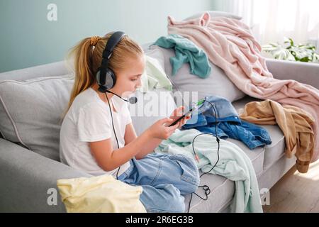 Une fille joue sur un téléphone portable. La chambre est en désordre. L'enfant a dispersé des choses dans la chambre. Banque D'Images