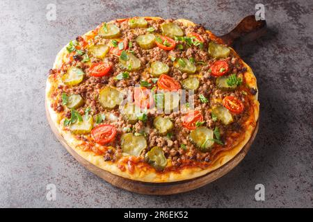 Tasty Pizza est recouvert d'une sauce crémeuse à hamburger, de bœuf haché, de fromage et de cornichons sur le panneau en bois de la table. Horizontale Banque D'Images