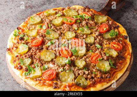 Cheeseburger Pizza est recouvert d'une sauce crémeuse à hamburger, de boeuf haché, de fromage et de cornichons sur le panneau en bois de la table. Horizontale Banque D'Images