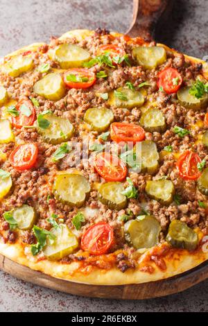 Pizza chaude avec bœuf haché, tomates, concombres marinés et fromage en gros plan sur une planche de bois sur la table. Verticale Banque D'Images