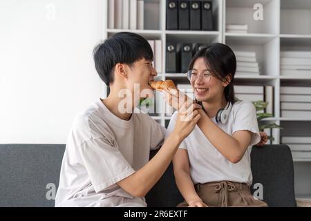 Les jeunes couples passent des vacances dans le salon. Le jeune homme portait des vêtements confortables, montrant son visage, satisfait du goût des collations Banque D'Images