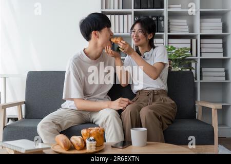 Les jeunes couples passent des vacances dans le salon. Le jeune homme portait des vêtements confortables, montrant son visage, satisfait du goût des collations Banque D'Images