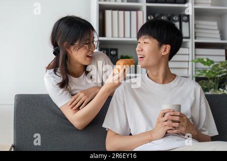 Les jeunes couples passent des vacances dans le salon. Le jeune homme portait des vêtements confortables, montrant son visage, satisfait du goût des collations Banque D'Images