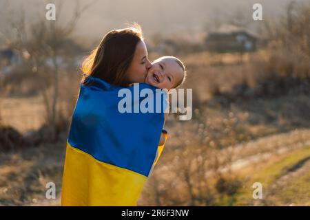 Une femme embrasse son petit fils enveloppé dans le drapeau jaune et bleu de l'Ukraine à l'extérieur. Banque D'Images